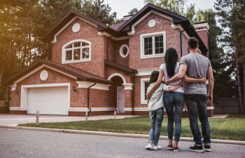 back view of a hugging family of three in front of a red-brick house