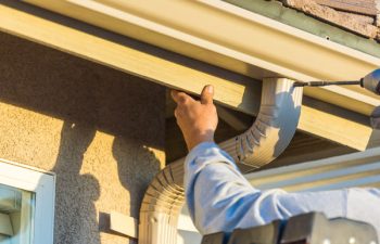 Worker Attaching Aluminum Rain Gutter and Down Spout to Fascia of House