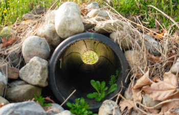 looking through a french drain with a black pipe and large rocks surrounding it